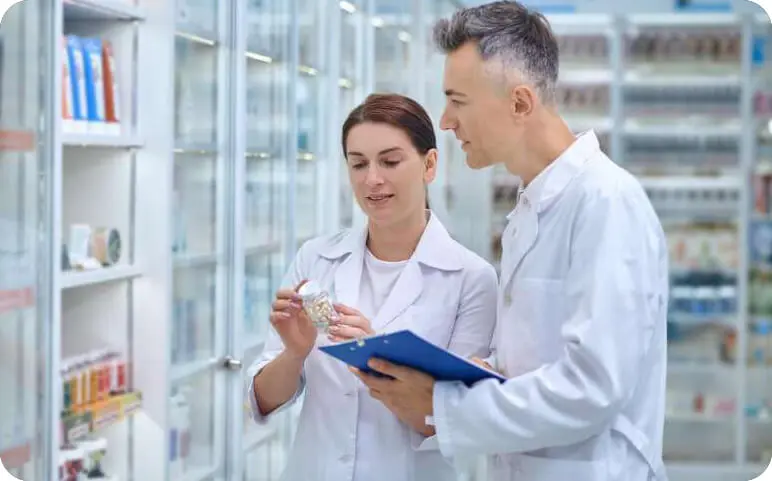 Two pharmacists discuss details of prescription medications among shelves of pharmaceuticals